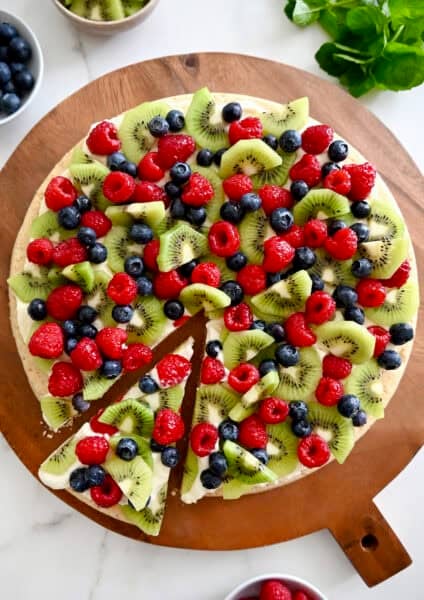 Fruit pizza with a sugar cookie crust and cream cheese frosting topped with fresh blueberries, raspberries and kiwi.