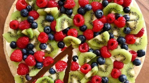 Fruit pizza with a sugar cookie crust and cream cheese frosting topped with fresh blueberries, raspberries and kiwi.