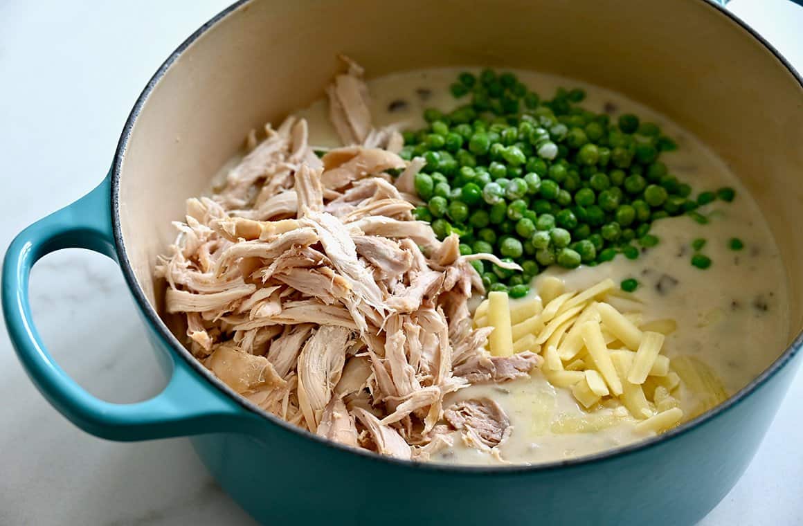A large stockpot containing shredded poultry, frozen peas, broth and shredded white cheddar cheese