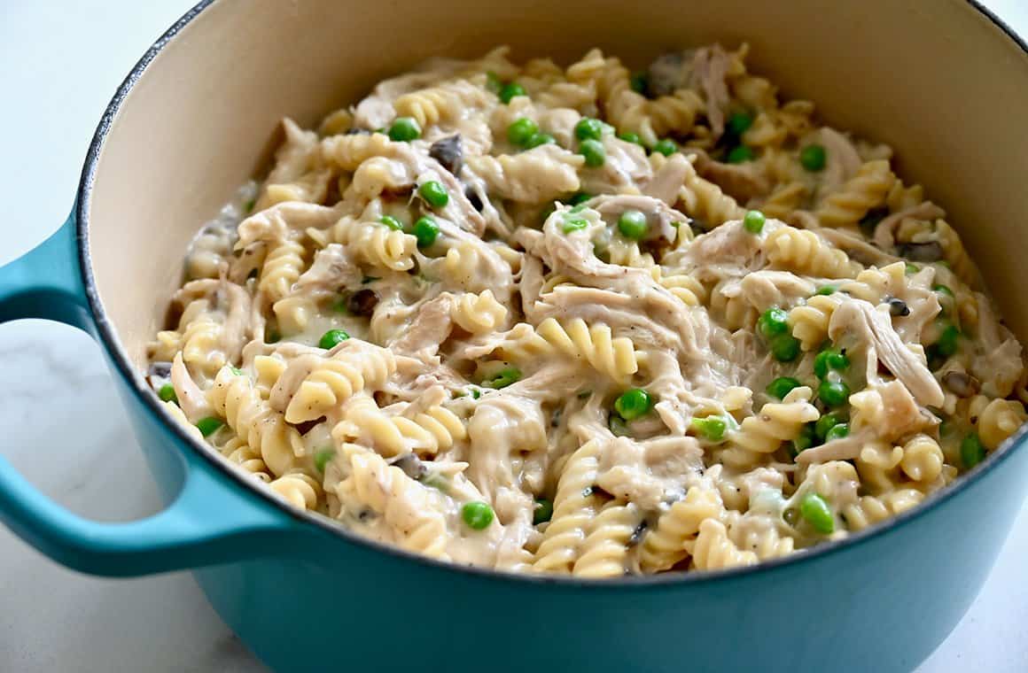 A large stockpot containing pasta, peas and shredded poultry in a creamy broth