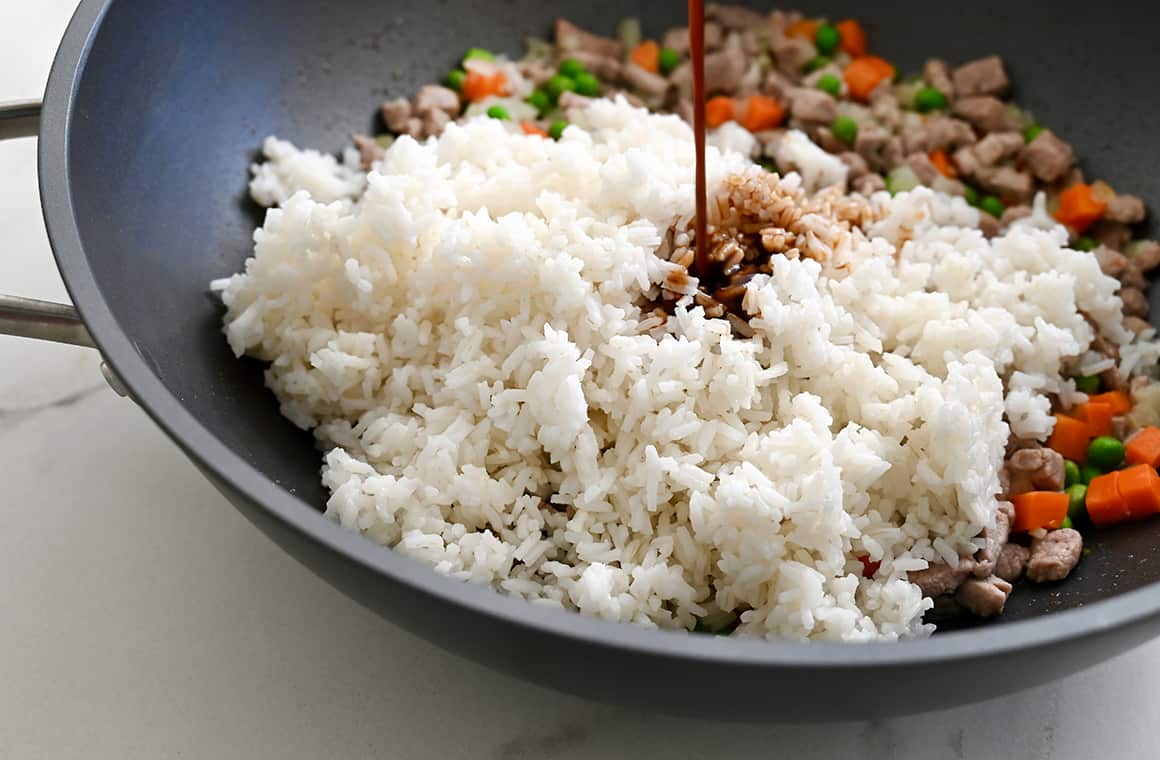 White rice in a large skillet with peas and carrots, which is all being drizzled with low-sodium soy sauce