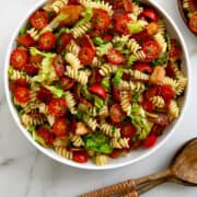 A top-down view of BLT Pasta Salad in a large white serving bowl next to wood serving utensils.