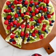 A top-down view of a fresh fruit pizza with a sugar cookie base atop a wood serving board.