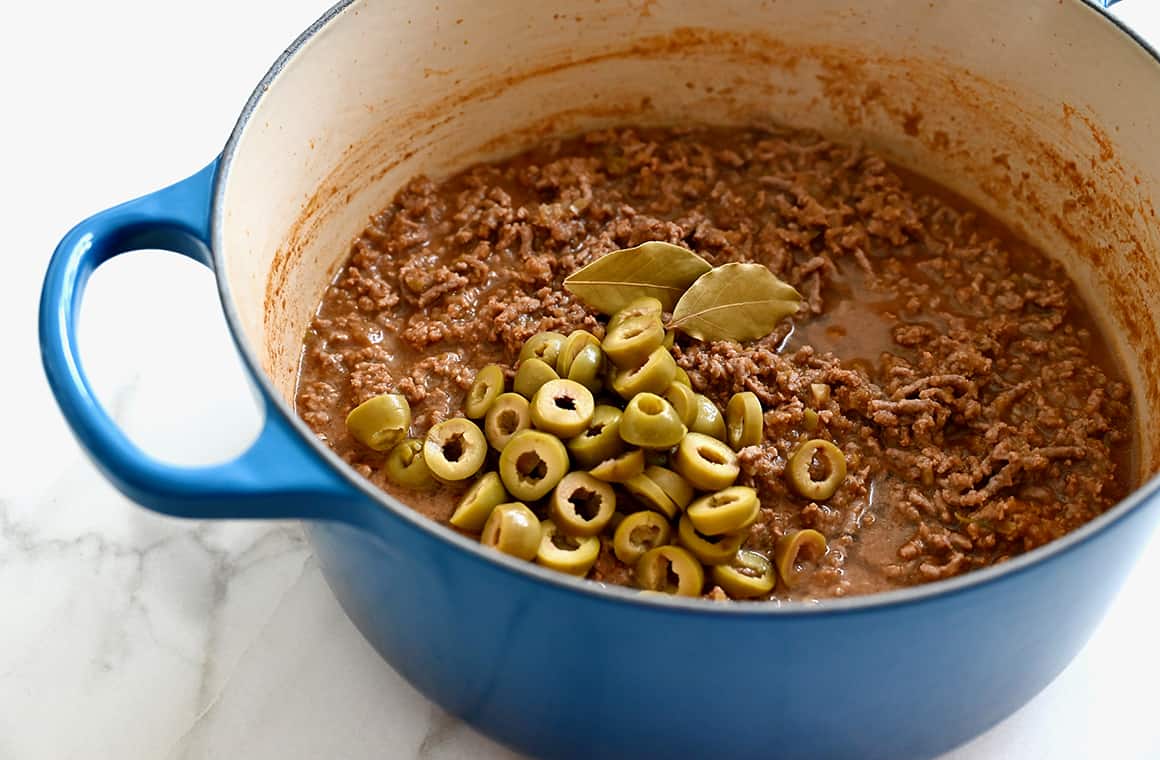 A large stockpot containing ground beef, green olives and two bay leaves