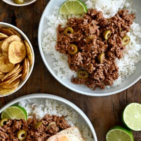 A top-down view of two plates containing white rice topped with Cuban Picadillo and a fried egg