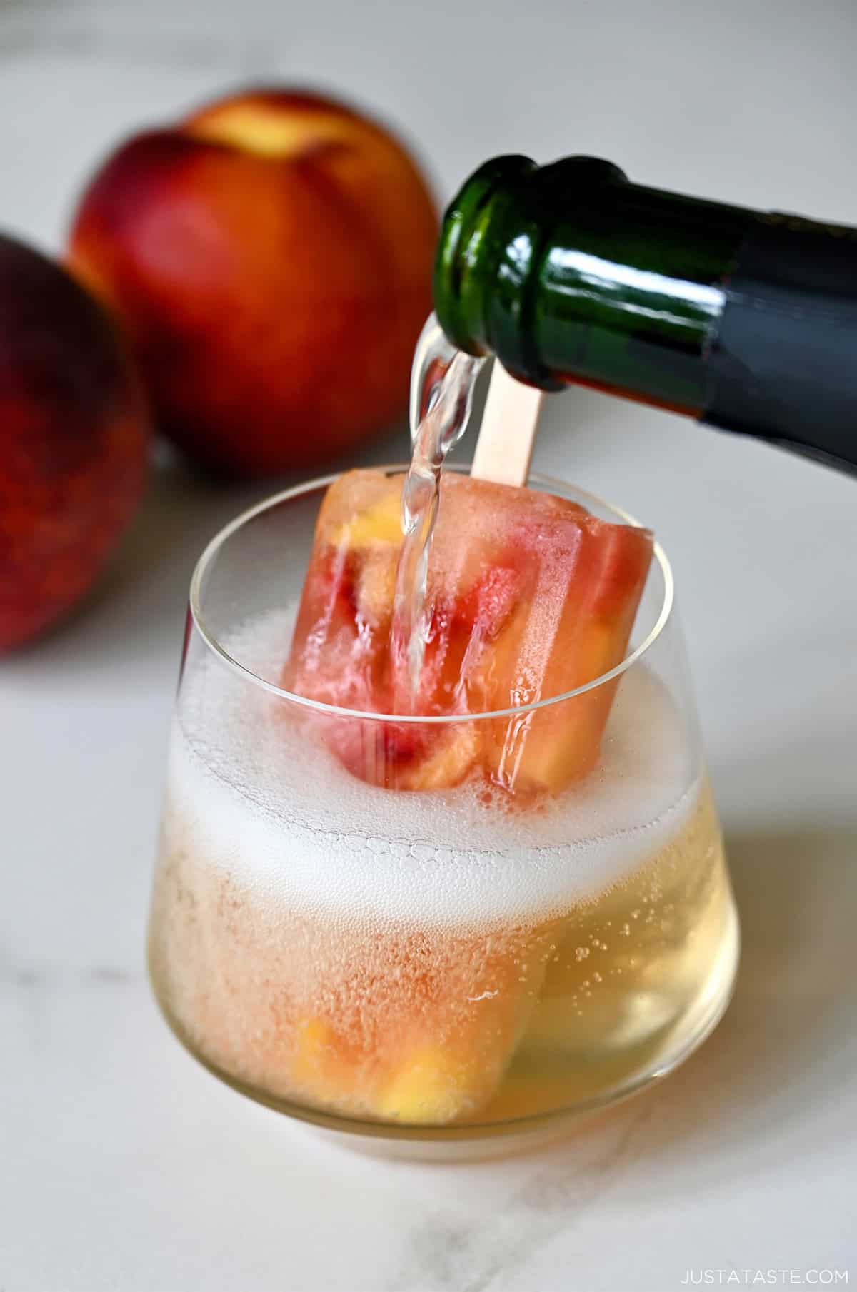 Peach sangria popsicle served in a wine glass topped with bubbly prosecco.