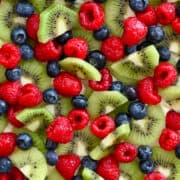 A close-up view of fresh kiwi, raspberries and blueberries atop cream cheese frosting.
