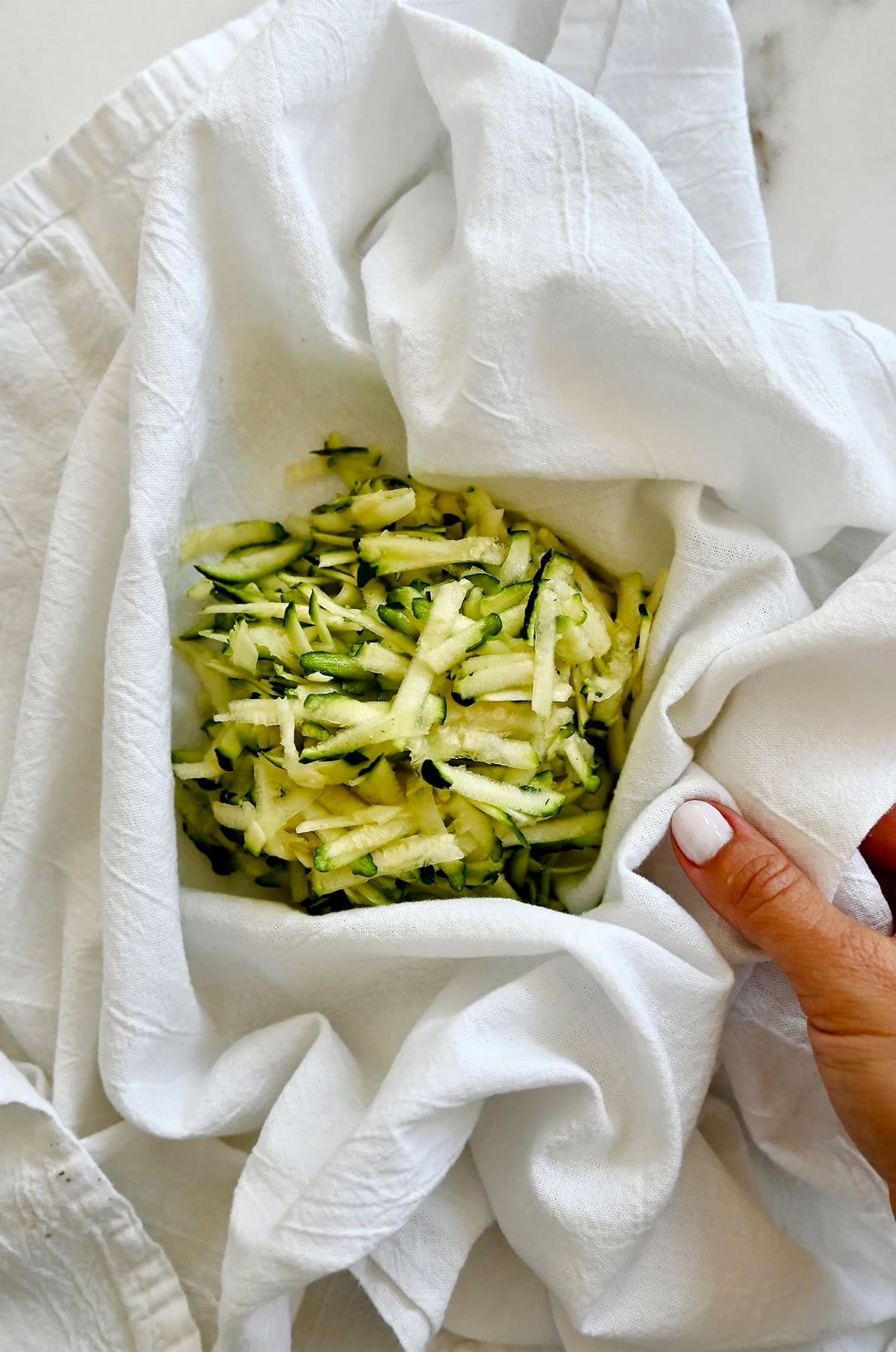 Shredded zucchini in a kitchen towel before wringing out excess liquid.