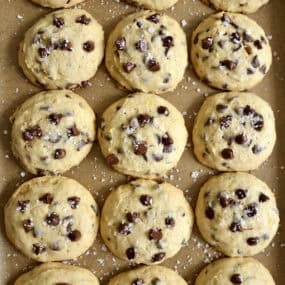 Banana chocolate chip cookies sprinkled with large-flake sea salt on a parchment paper-lined baking sheet.