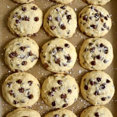 Banana chocolate chip cookies sprinkled with large-flake sea salt on a parchment paper-lined baking sheet.