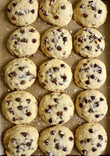 Banana chocolate chip cookies sprinkled with large-flake sea salt on a parchment paper-lined baking sheet.