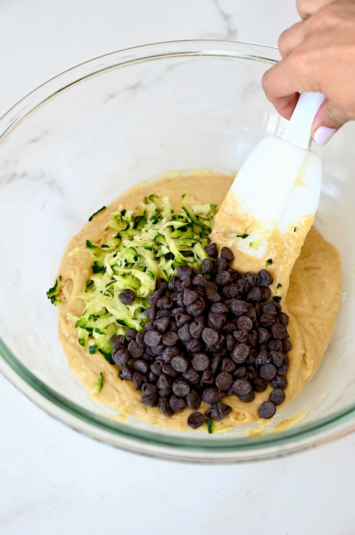 Folding in shredded zucchini and chocolate chips into muffin batter.