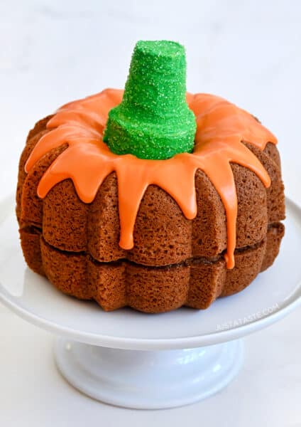 Easy Pumpkin Bundt Cake topped with a thick orange-colored glaze and a green sugar cone "stem" on a cake platter