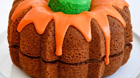Easy Pumpkin Bundt Cake topped with a thick orange-colored glaze and a green sugar cone "stem" on a cake platter