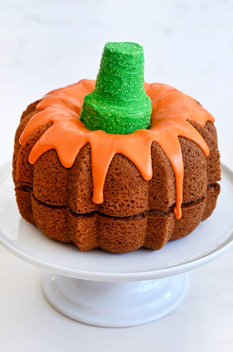 Easy Pumpkin Bundt Cake topped with a thick orange-colored glaze and a green sugar cone "stem" on a cake platter 