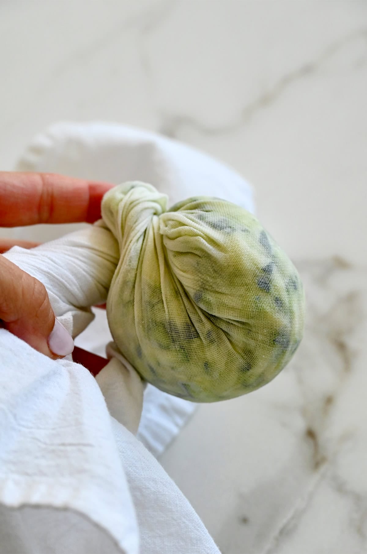 Removing excess liquid from shredded zucchini wrapped in a kitchen towel.