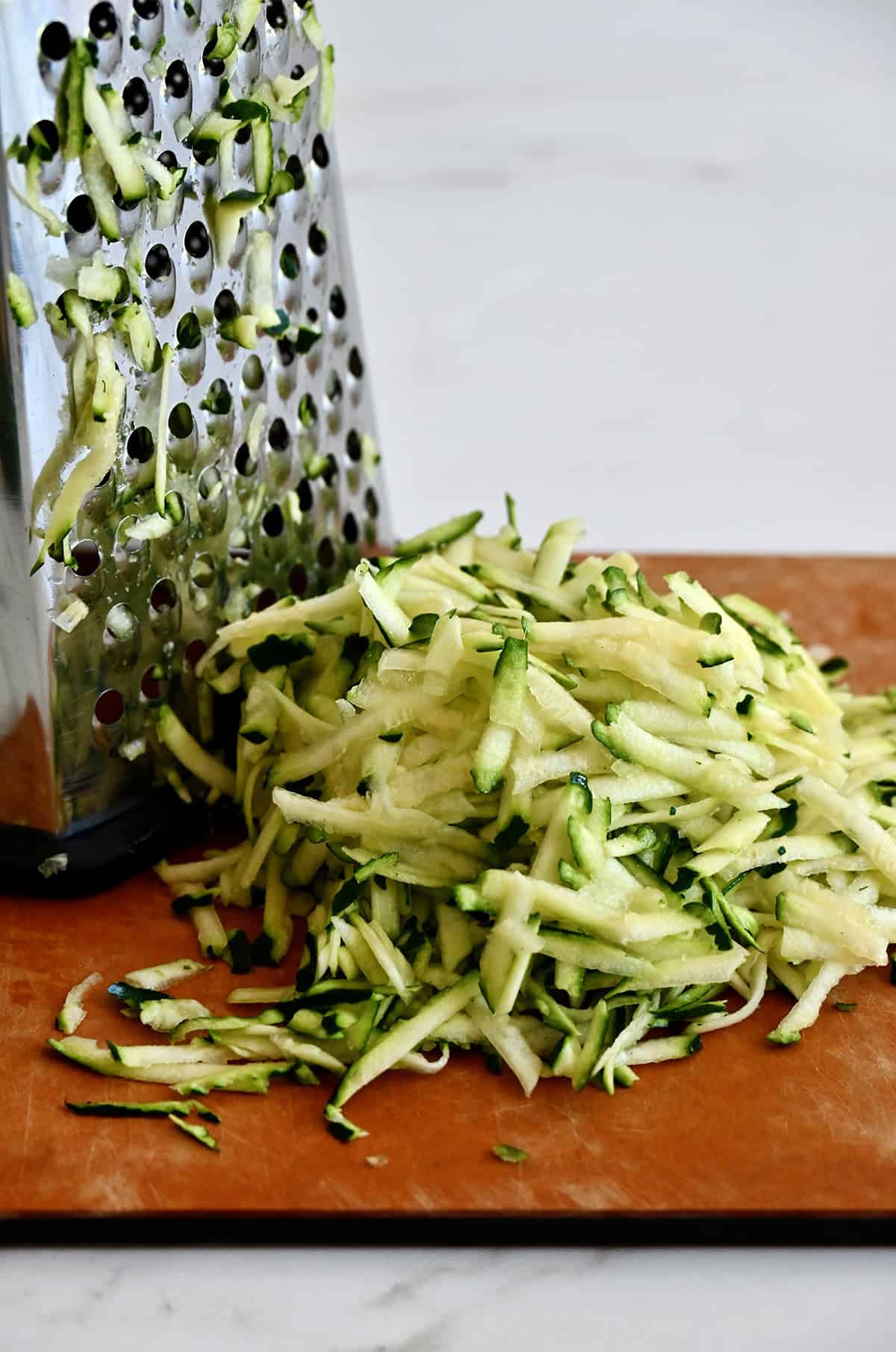 A pile of shredded zucchini is next to a box grater.