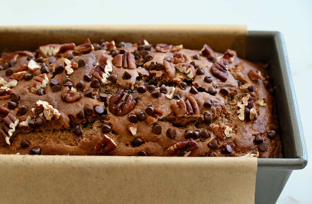 Freshly baked healthy banana bread with mini chocolate chips and chopped pecans in a loaf pan lined with parchment paper.