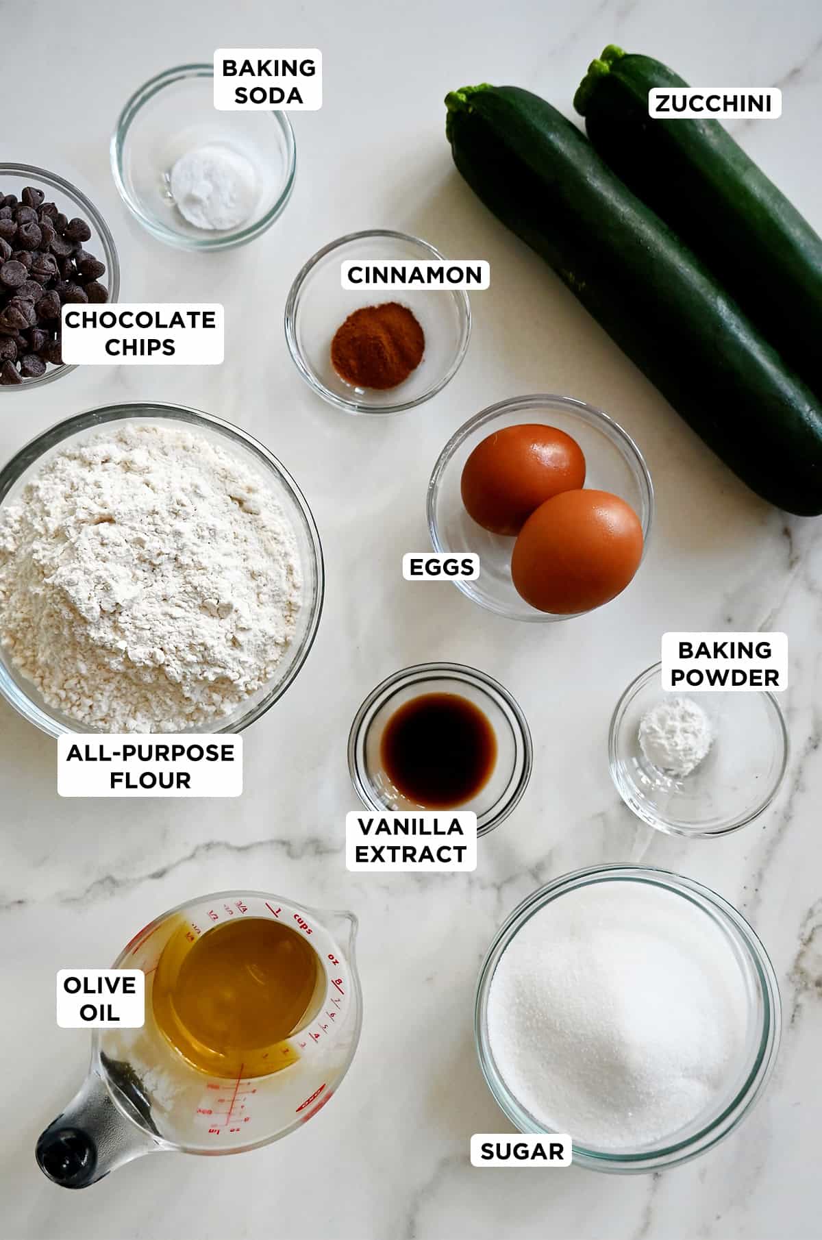 All the ingredients needed to make zucchini muffins with chocolate chips, in various-sized prep bowls.