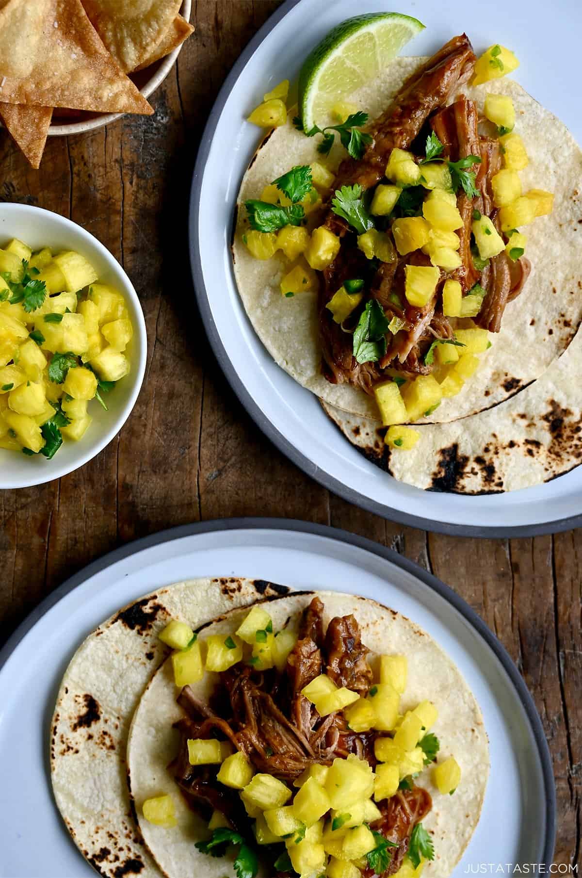 Hawaiian pulled pork tacos with fresh pineapple chunks and cilantro near a bowl with homemade tortilla chips.