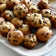 Mini Chocolate Chip Banana Muffins on a white serving platter next to a bunch of ripe bananas.