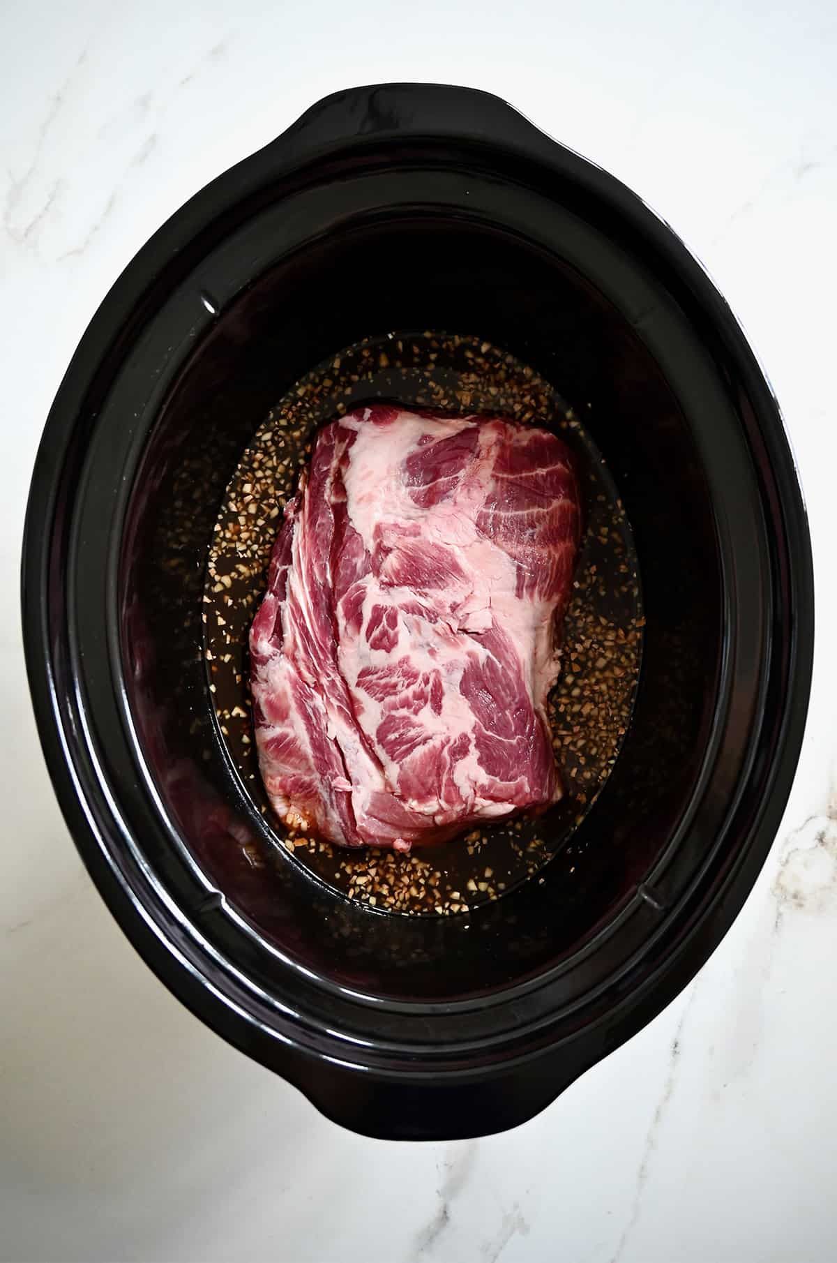 A pork butt in a slow cooker with a homemade sweet and tangy sauce.
