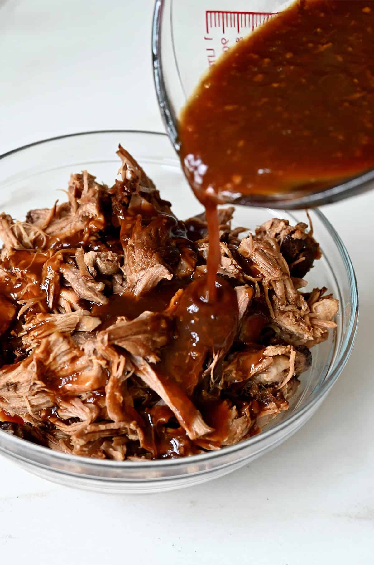 Pouring a sticky pineapple soy sauce over pulled pork in a bowl.