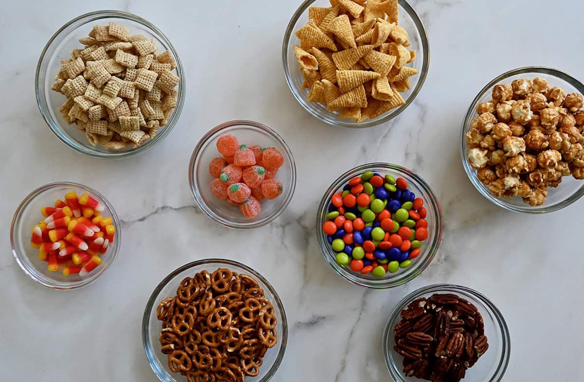 Glass bowls containing sweet and salty snacks to make up a cereal party mix.