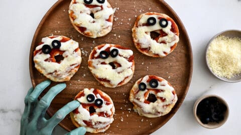 A wood platter with mini bagel pizzas and a green mummy hand