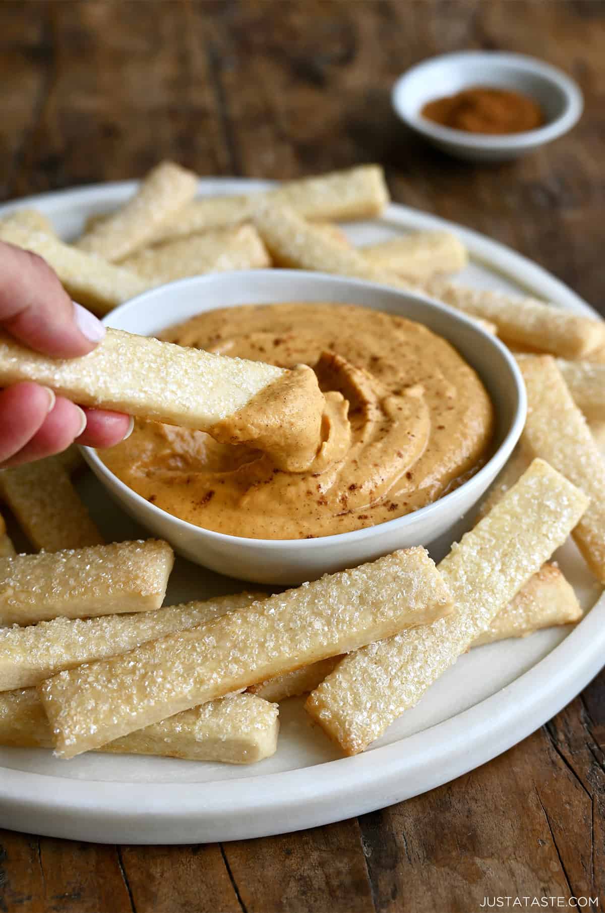 Hand dipping a pie crust fry into creamy pumpkin dip.
