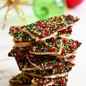 A tall stack of Christmas Saltine Cracker Toffee in front of holiday ornaments