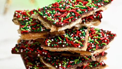 A tall stack of Christmas Saltine Cracker Toffee in front of holiday ornaments