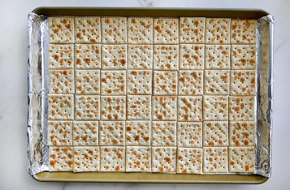 A top-down view of saltine crackers atop a aluminum foil-lined baking sheet