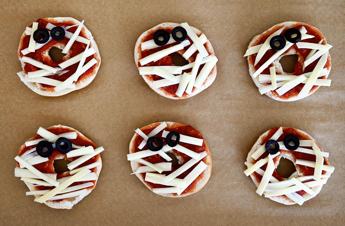 Unbaked mini bagel mummy pizzas on brown parchment paper