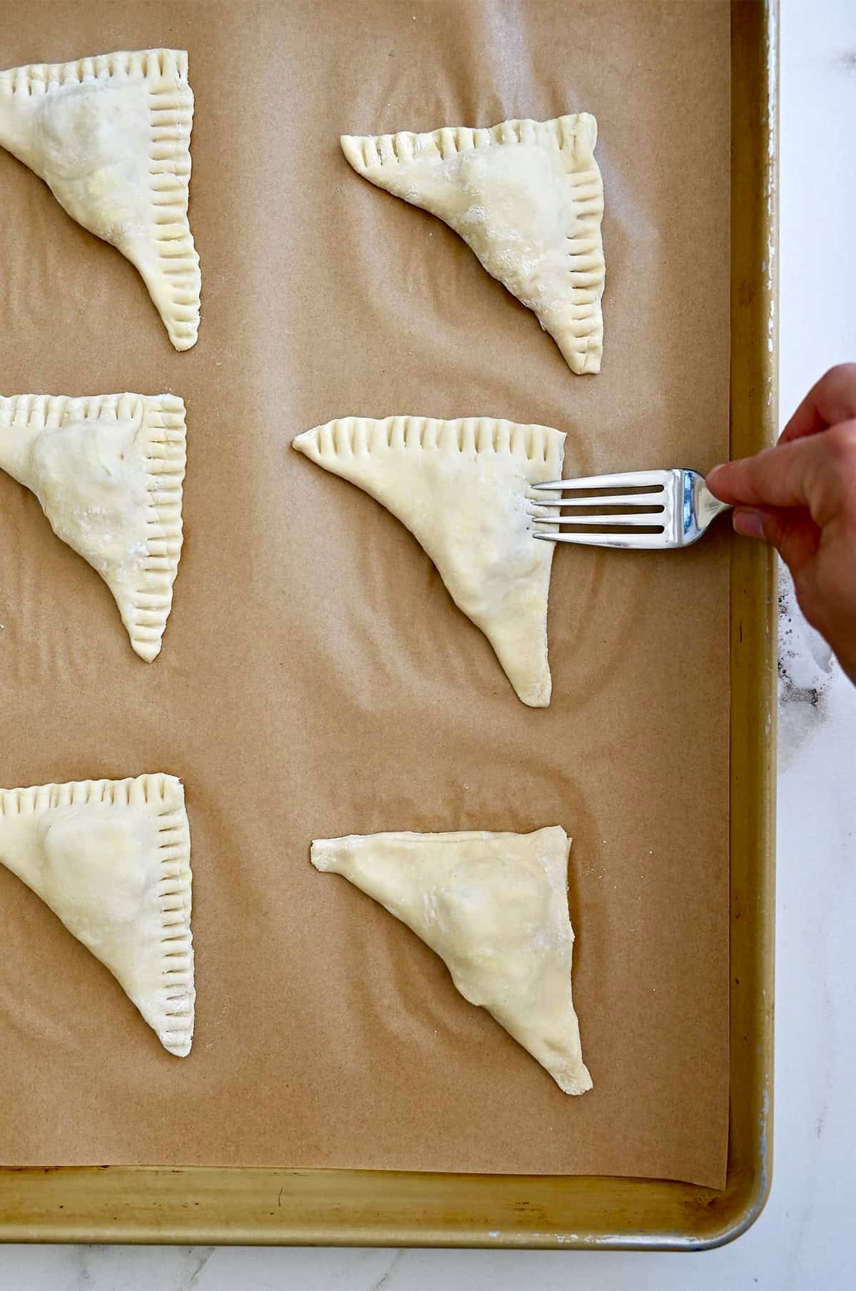 Using a fork to crimp the edges of a puff pastry pocket stuffed with Brie, jam and nuts.