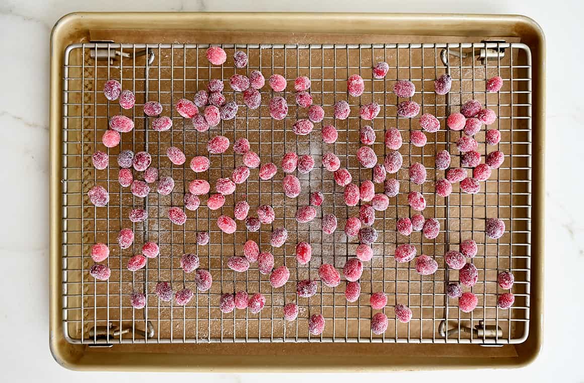 A top-down view of frosted cranberries drying atop a wire rack on a baking sheet