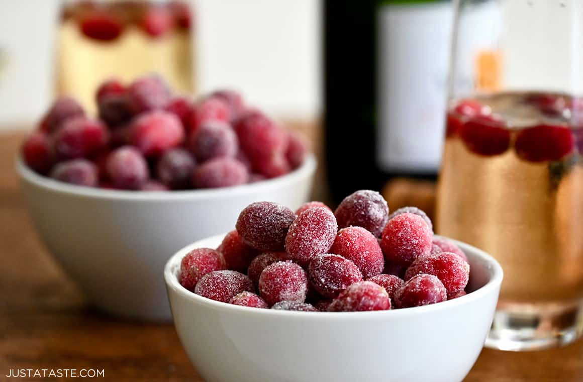 Festive candied cranberries piled high in a small bowl next to a glass of sparkling wine 