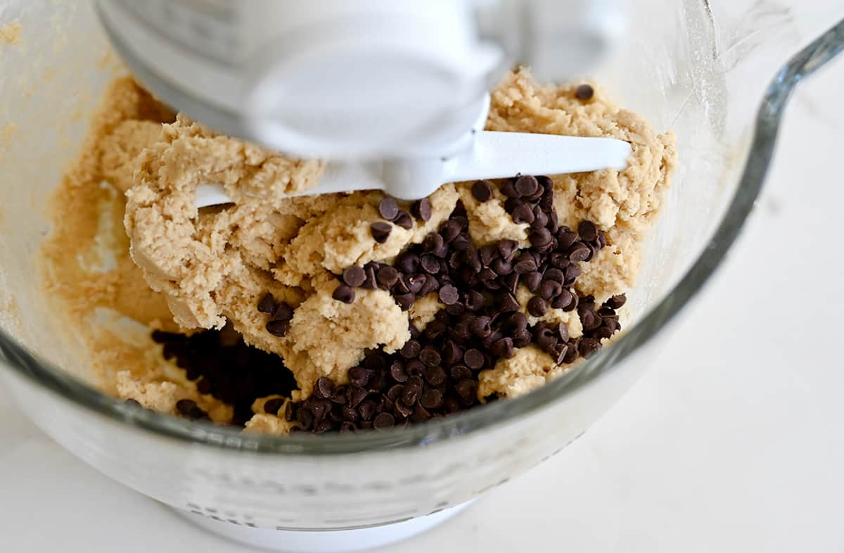 Cookie dough and mini chocolate chips in a stand mixer bowl with the paddle attachment.