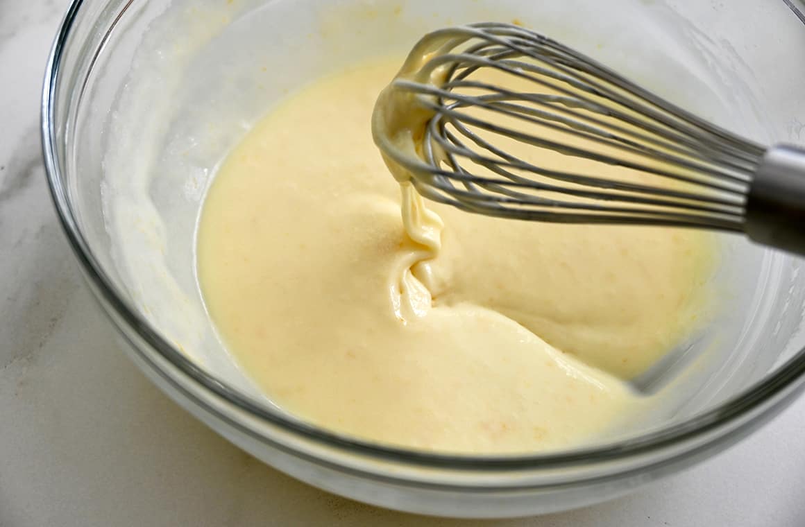 A whisk above a clear bowl containing homemade orange glaze