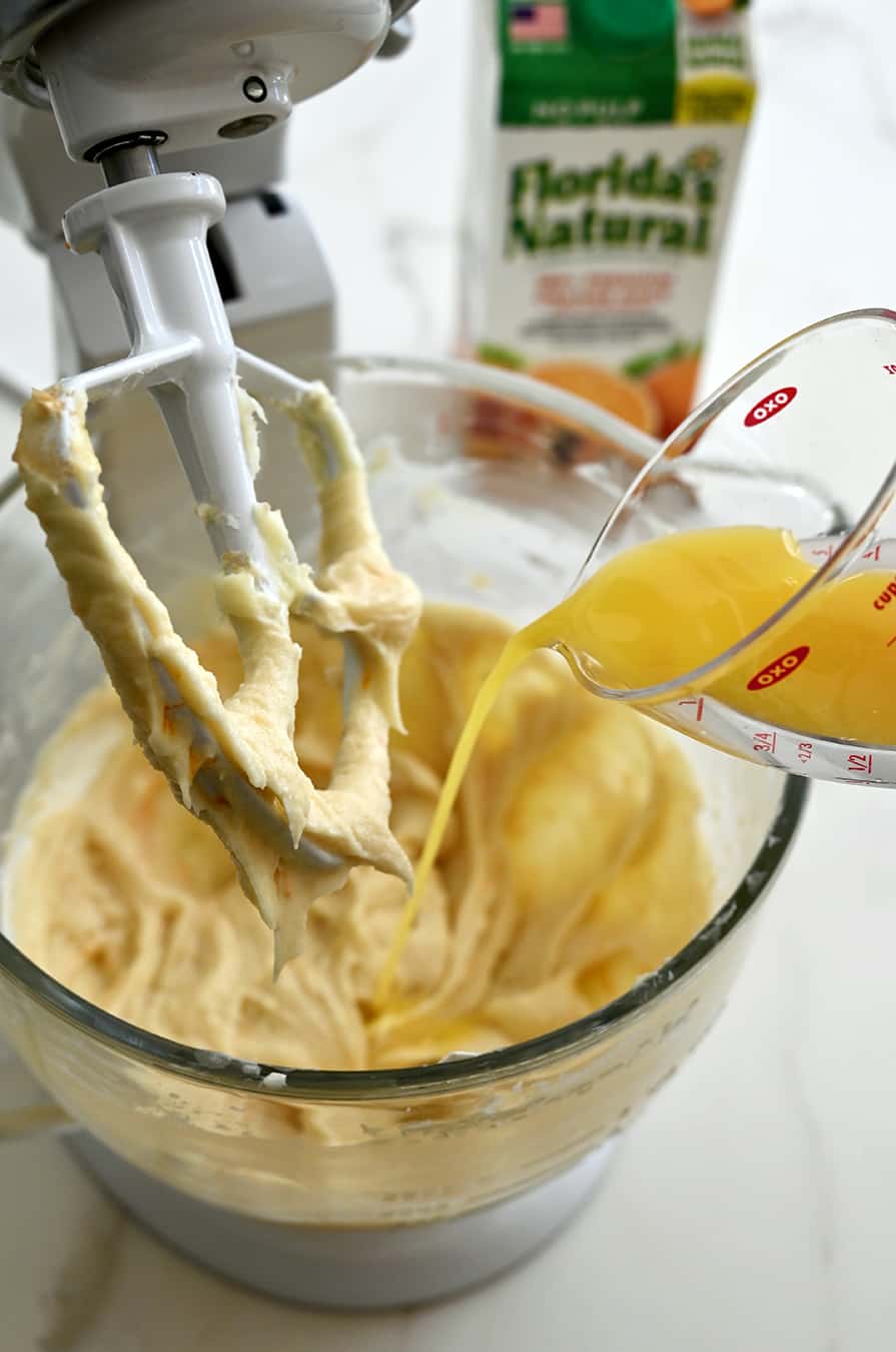 Juice being poured atop cake batter in a bowl of a stand mixer