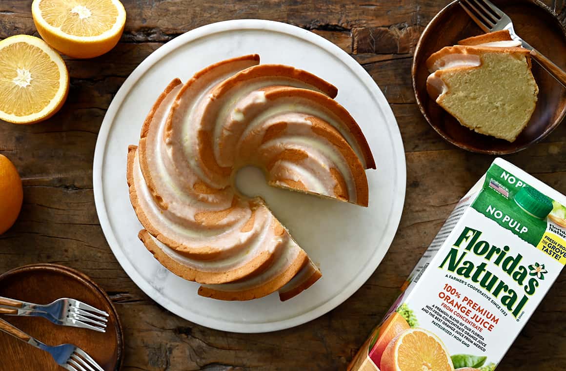 A top-down view of an orange bundt cake on a round cake plate next to a slice of cake on a plate