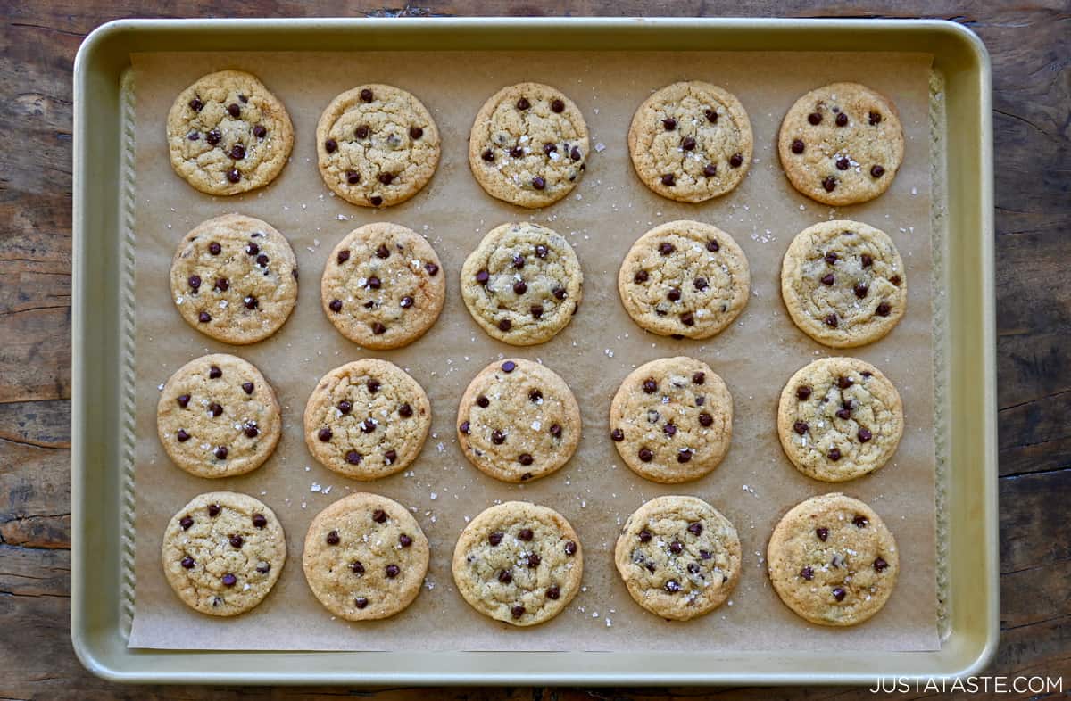 Perfect rows of mini chocolate chip cookies sprinkled with sea salt on a parchment paper-lined baking sheet.