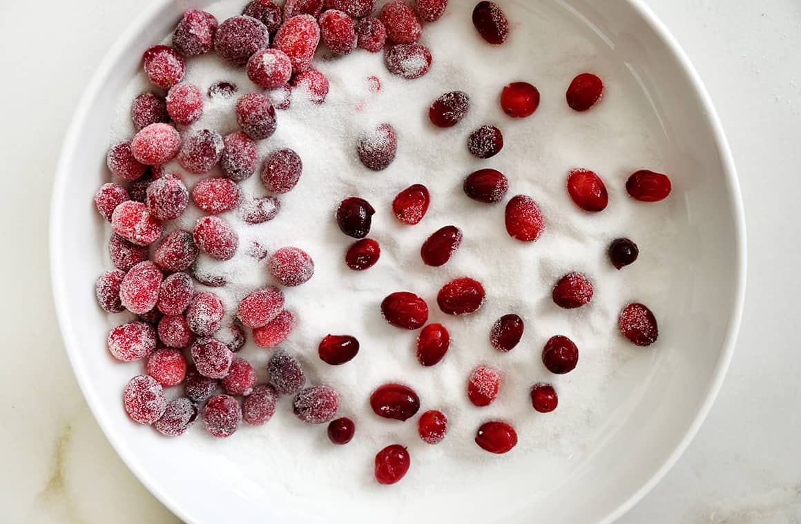 A top-down view of a large white bowl containing sugar and fresh cranberries