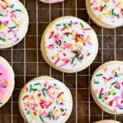A top-down view of sugar cookies with pink and white icing and rainbow sprinkles.