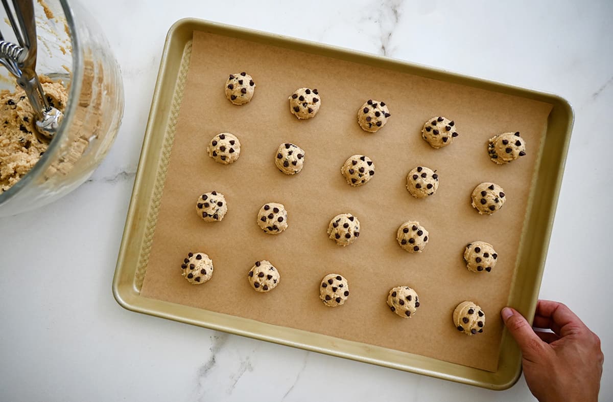 Balls of cookie dough studded with mini chocolate chips on a parchment paper-lined baking sheet.