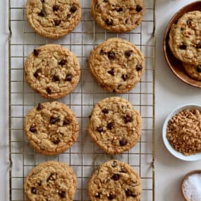 Toffee chocolate chip cookies garnished with large-flake sea salt cooling on a wire baking rack.