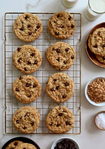 Toffee chocolate chip cookies garnished with large-flake sea salt cooling on a wire baking rack.