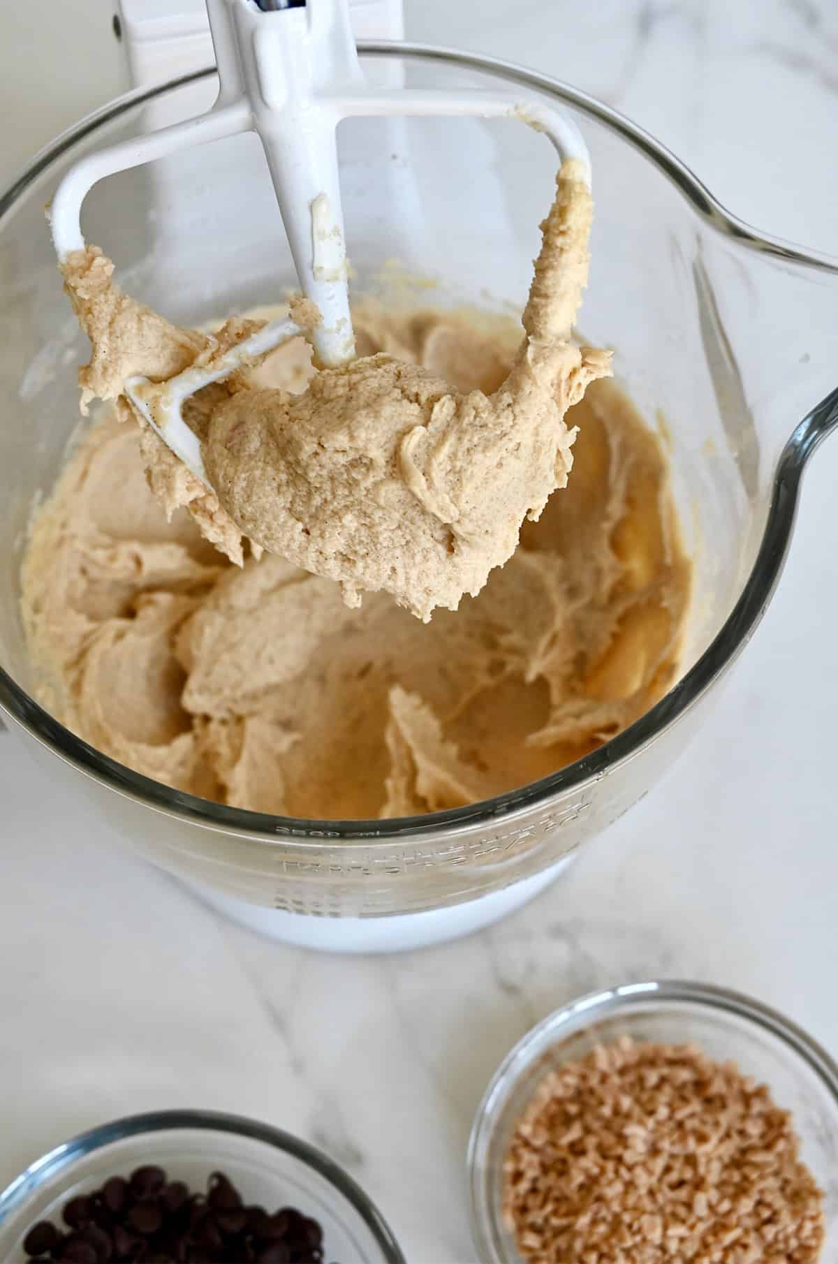 A butter, sugar and egg mixture covering a paddle attachment of a stand mixer.