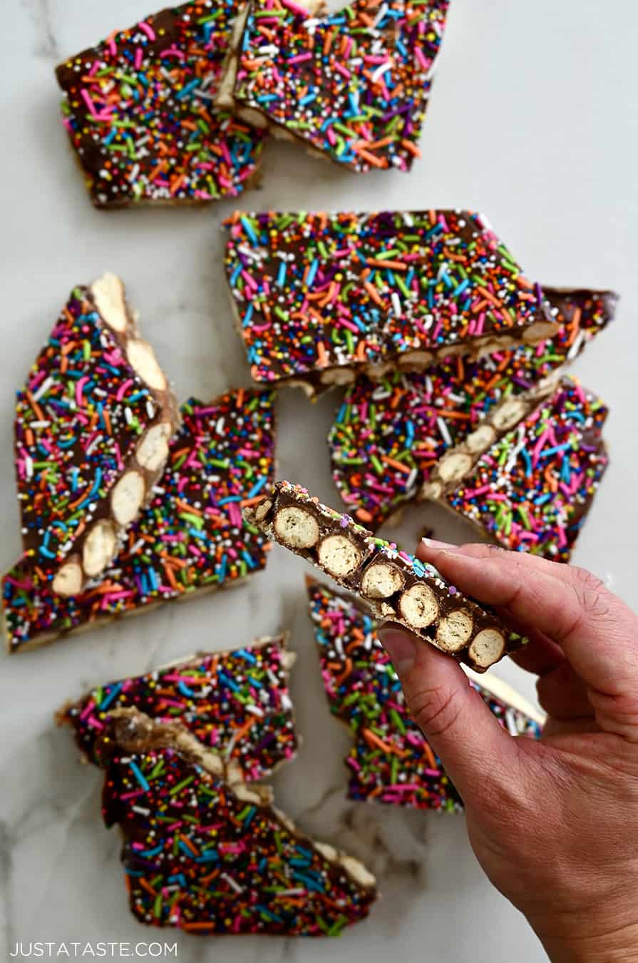 A hand holding a piece of pretzel bark topped with rainbow sprinkles