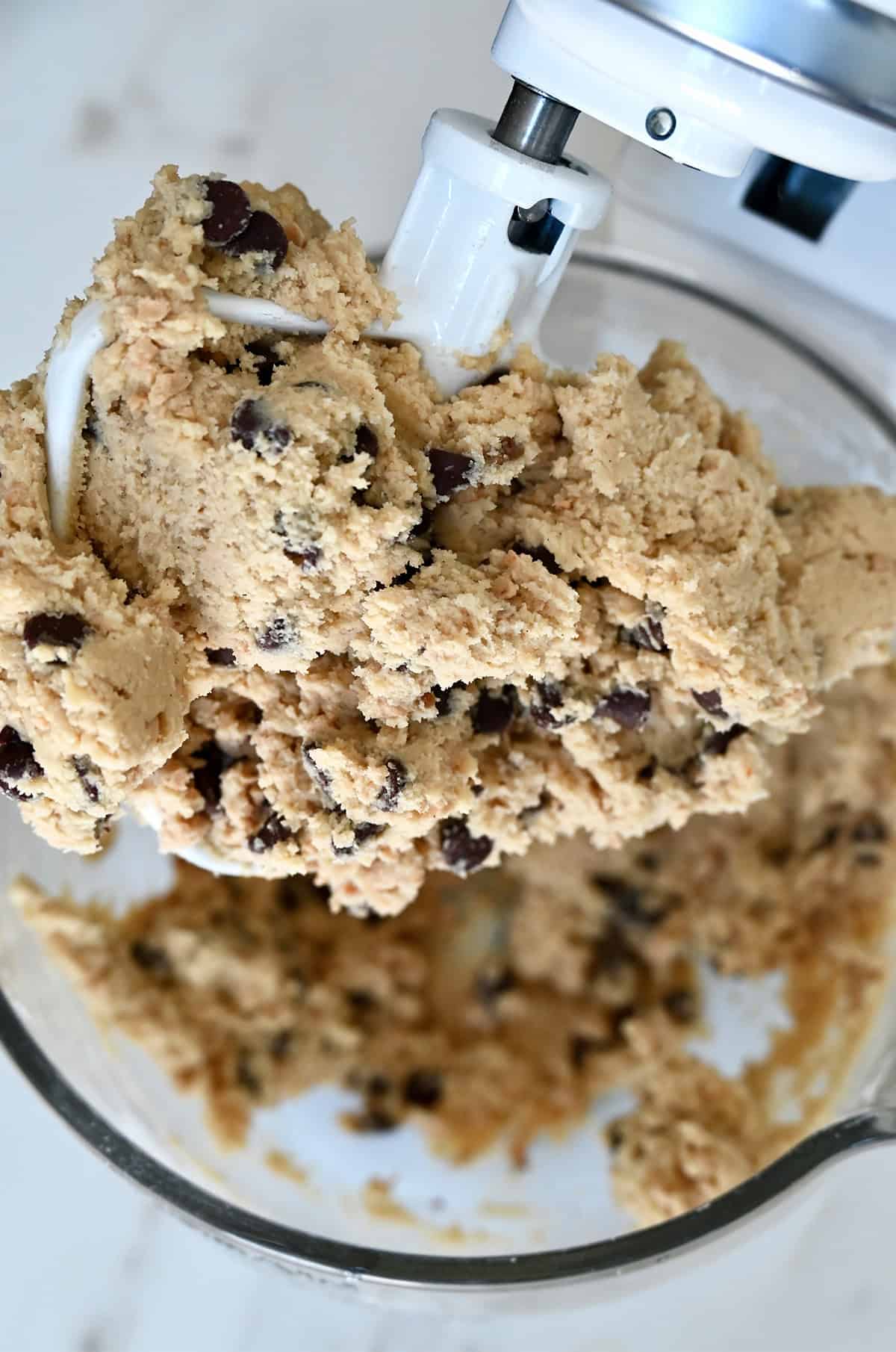 The paddle attachment of a stand mixer covered in toffee chocolate chip cookie dough.